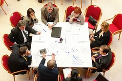 9 people sit around a table and discuss which projects are suitable for funding.