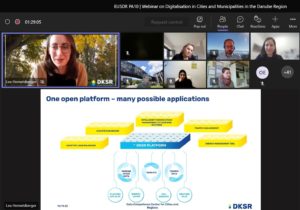 Smart Village Webinar: Zoom Meeting interface showing the speaker Lea Hemetsberger on the left. The shared Powerpoint Presentation is right below the row of participants. The slide has the title "One open platform - many possible applications" and shows a yellow and blue graphic of the DKSR platform that collects data in a climate dashboard, energy management tool, traffic management tool and adaptive load balancing. The graphic shows that the platform collects data such as floating car data, energy usage, weather data and CO2 sensor data.